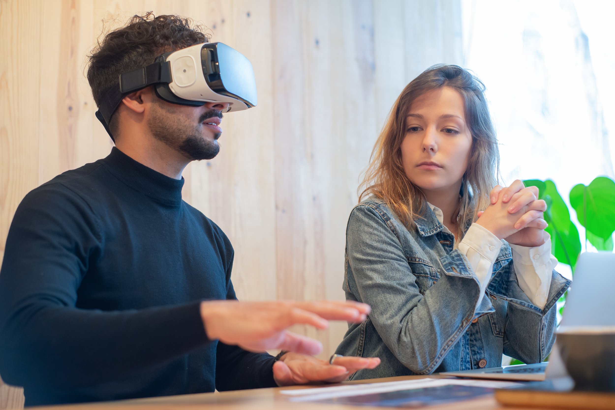 A woman sitting besides a man wearing vr goggles